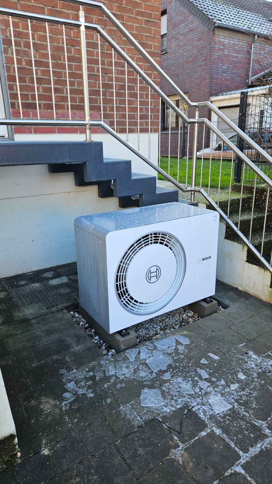 Bosch-Wärmepumpe im Außenbereich unter Treppe, umgeben von Eisplatten auf dem Boden – sichtbar nach Frost.